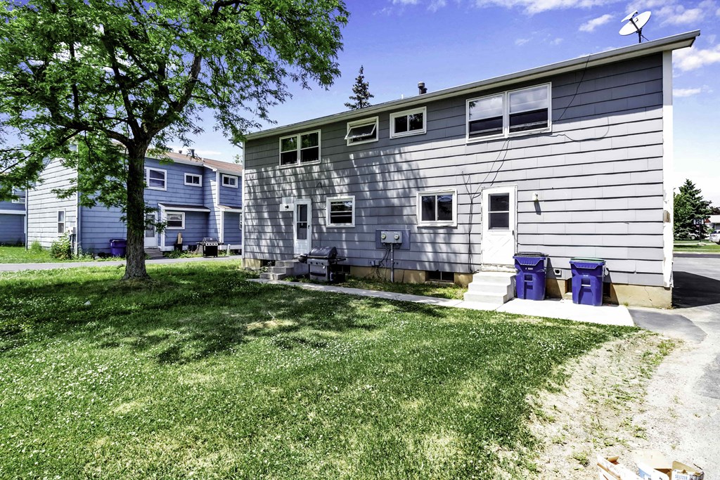 the front of a white house with blue chairs and a tree