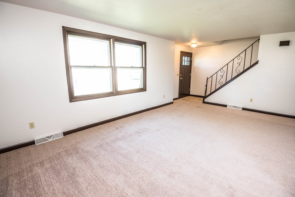 the living room and entryway of an empty house with carpet and a large window
