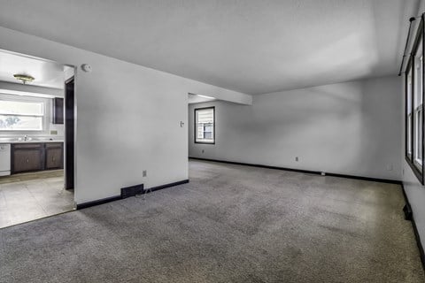 the living room and kitchen of a new home with white walls and carpet
