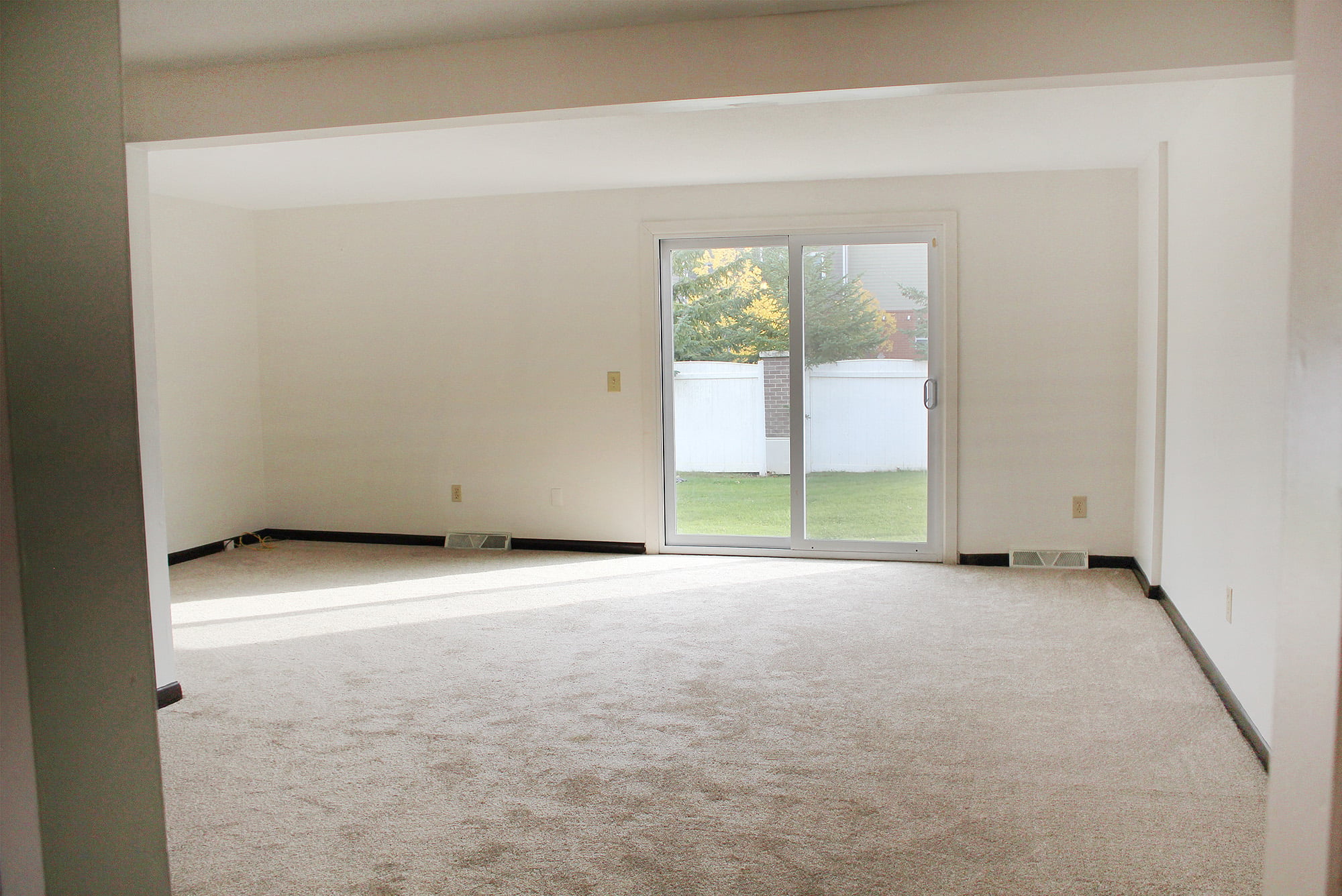 an empty living room with a white carpet and a glass door