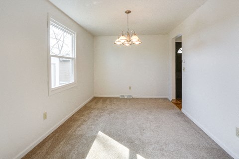 A room with a carpet, a window, and a chandelier.
