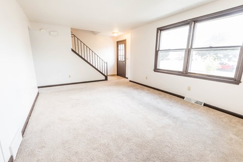 the living room and dining room of an empty home with large windows and carpeting