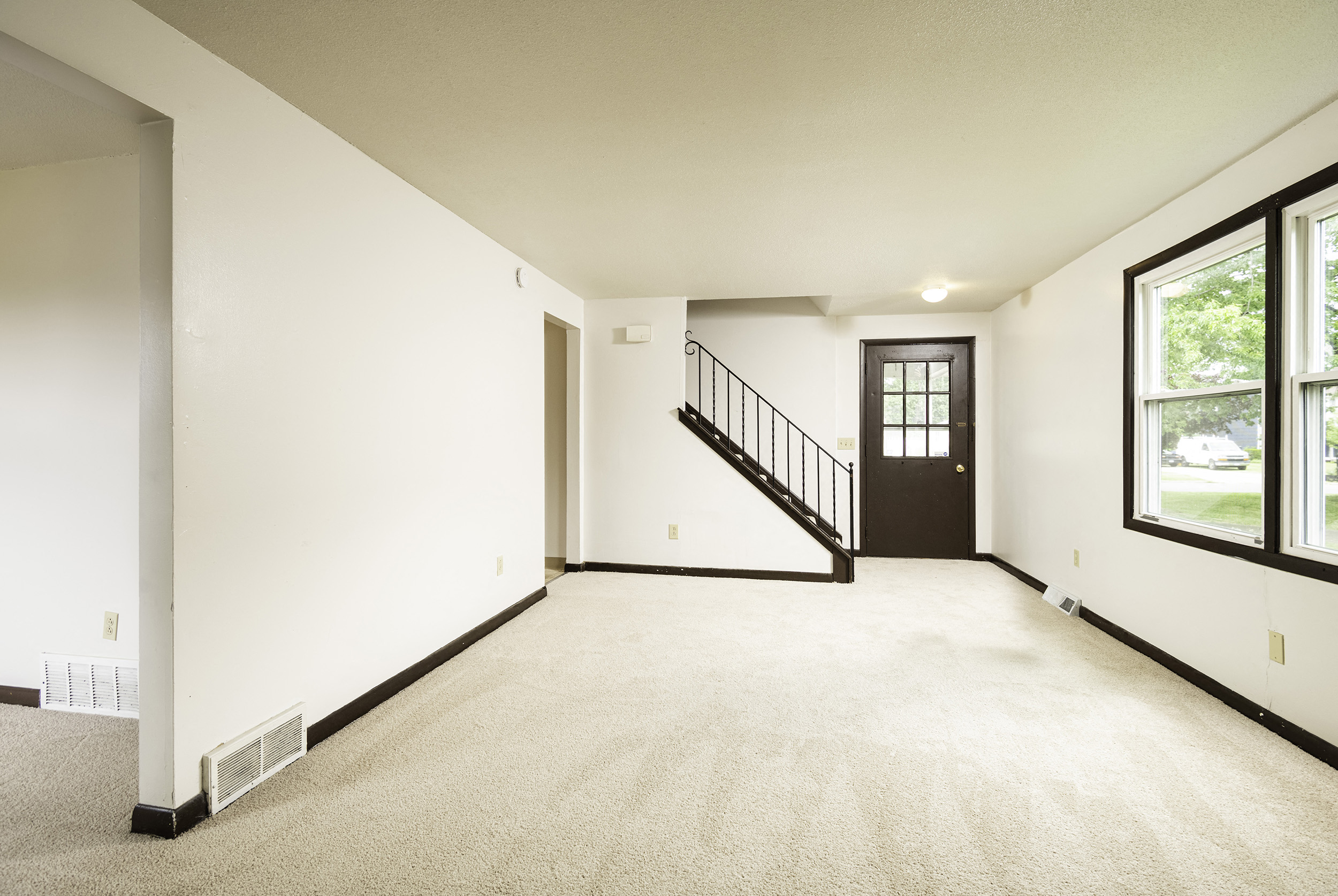 the living room of a house with white walls and a carpeted floor