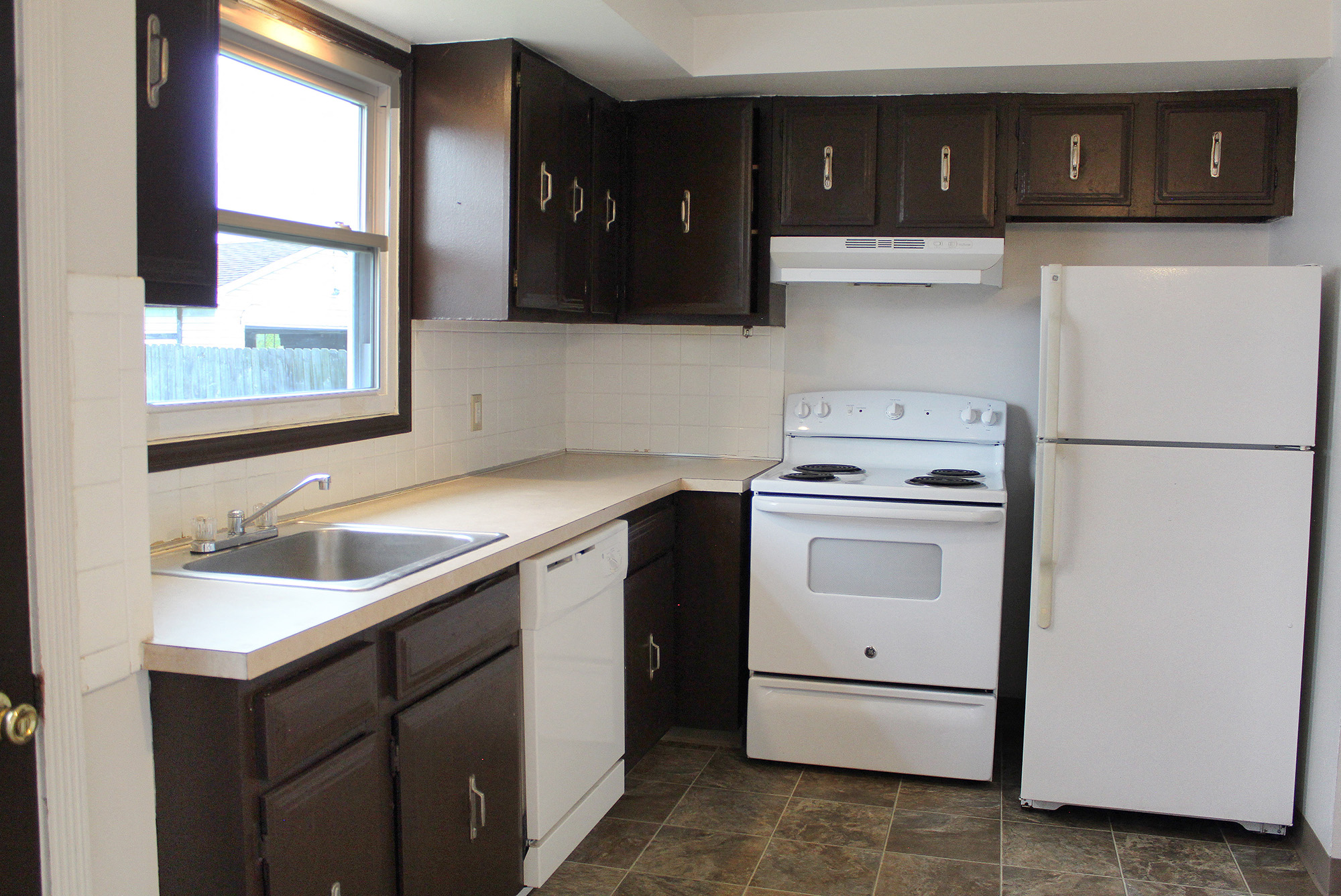 an empty kitchen with white appliances and dark cabinets