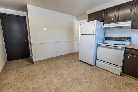 A kitchen with a white refrigerator, black door, and brown cabinets.