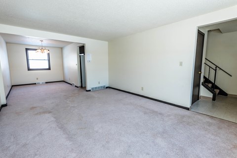 A spacious room with a window and a staircase.