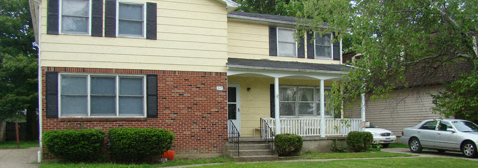 a yellow house with a white porch and a white car parked in front of it