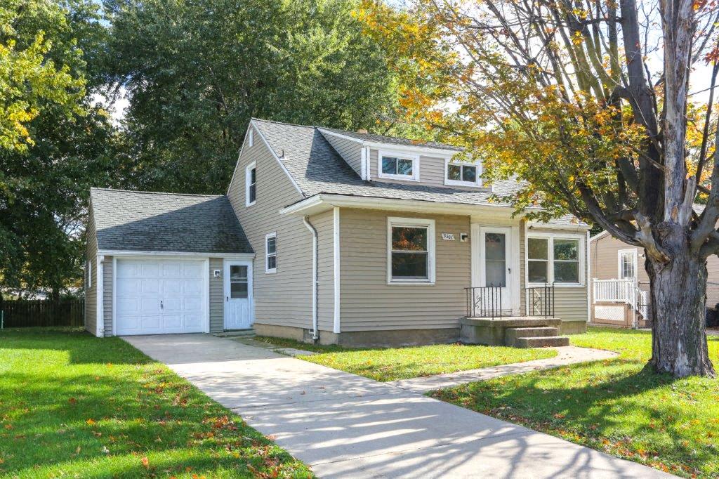 a tan house with a white garage and a sidewalk