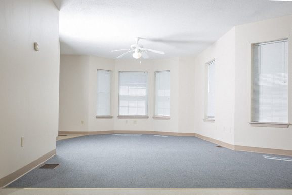 A spacious room with a carpeted floor and a ceiling fan.