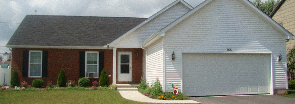 A white house with a garage door and a brick wall.
