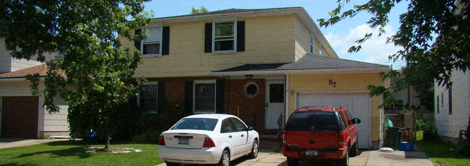 A white car is parked in front of a yellow house.