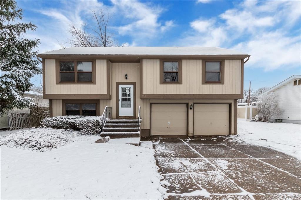 a tan house with a garage in the snow