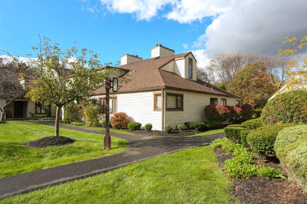 A house with a brown roof and white walls is surrounded by a well-manicured lawn and a clear sky.