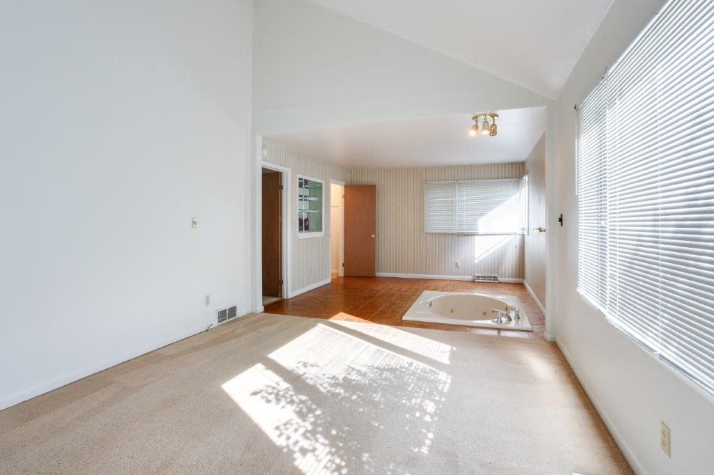 A sunny day in a spacious room with a bathtub and a window with blinds.