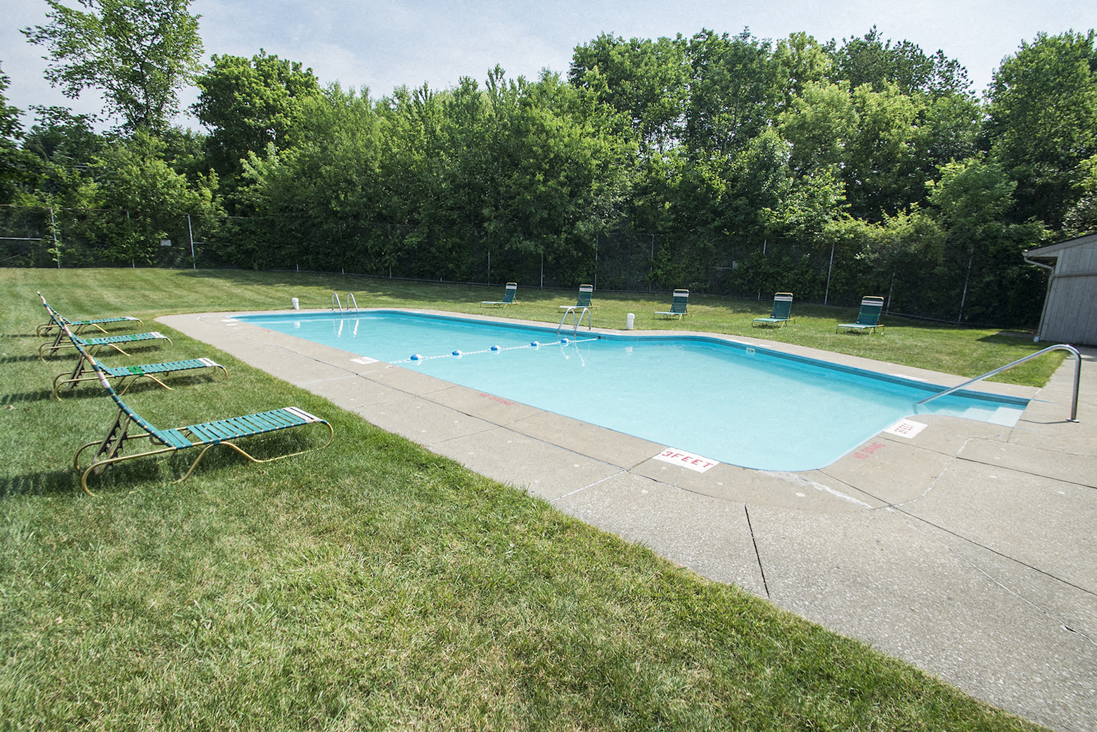 a swimming pool in the grass with chairs around it