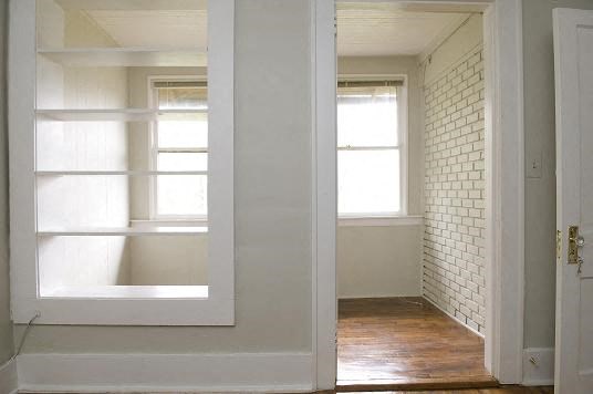 an empty room with a white door and two windows