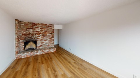an empty living room with a brick fireplace and wooden floors