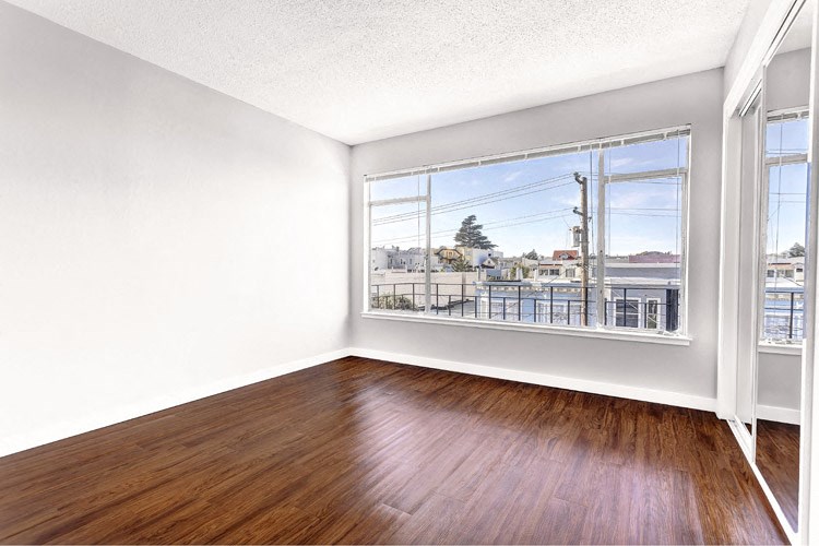 an empty living room with a large window and wood floors