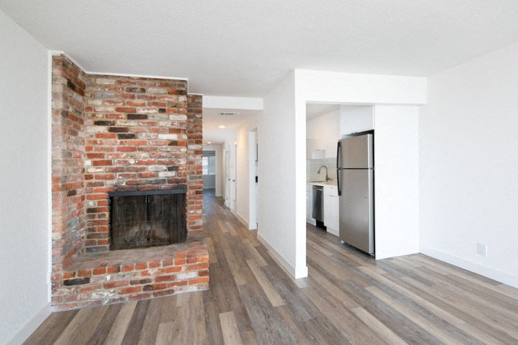 an empty living room with a brick fireplace and a kitchen
