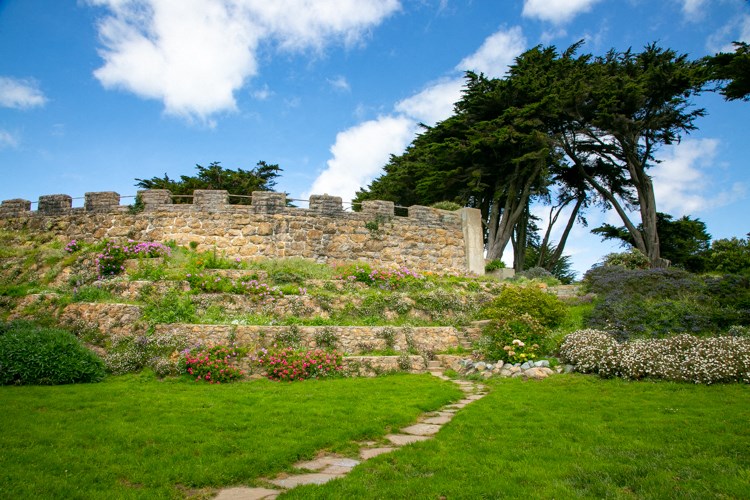 a path leading up to a stone wall with flowers and trees