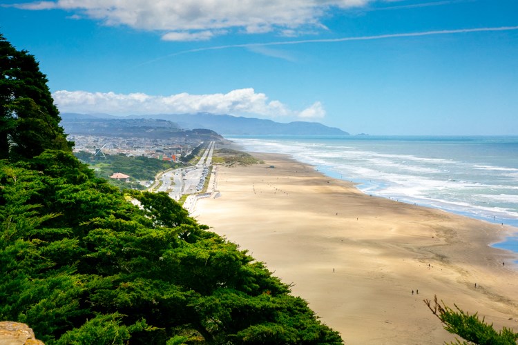 a view of the beach and the ocean from the top of a hill