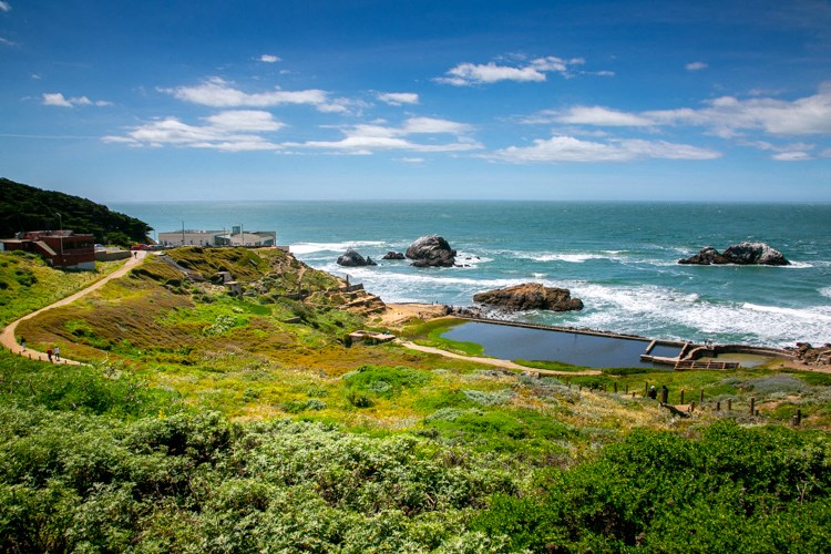 a pool of water next to the ocean with rocks in the water