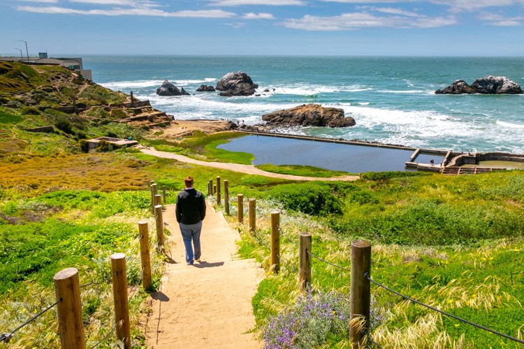 a man walking down a path to the ocean