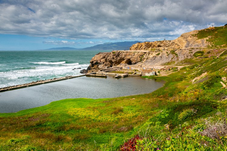 a small body of water next to a cliff with the ocean