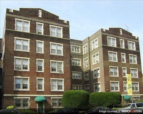 A brick building with a green awning and bushes in front.