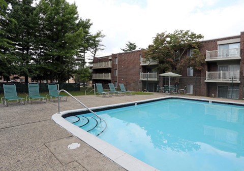 A swimming pool surrounded by chairs and trees in front of apartment buildings.