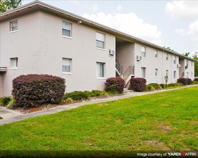 a white building with a green lawn and bushes