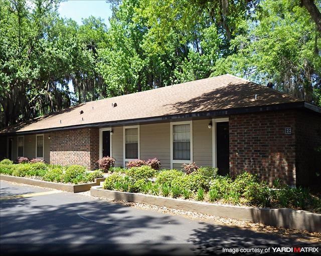 a small brick house with bushes and trees
