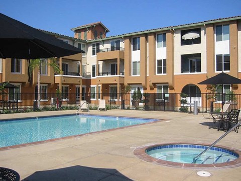 A large swimming pool in front of a building with a black umbrella.