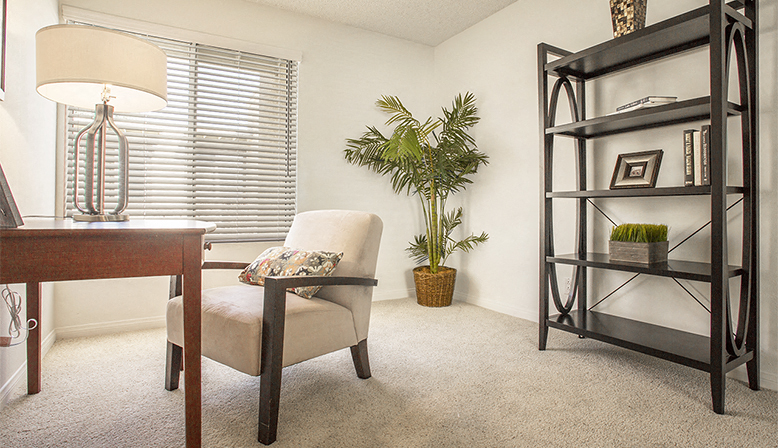 a living room with a chair and a desk and a book shelf