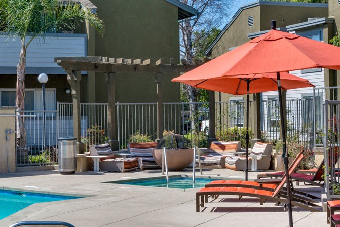 a poolside patio with chairs and umbrellas next to a swimming pool
