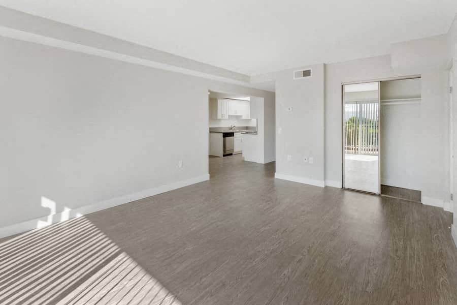 an empty living room with a sliding glass door to a kitchen