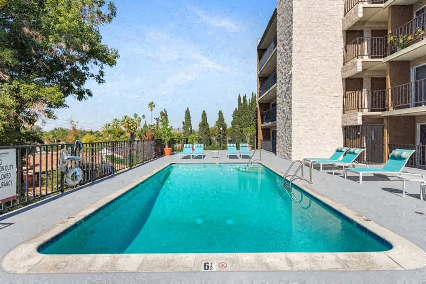 a swimming pool with blue chaise lounge chairs and a building in the background