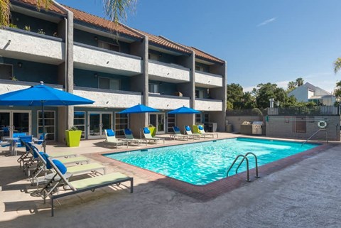 a swimming pool with chairs and umbrellas in front of a hotel
