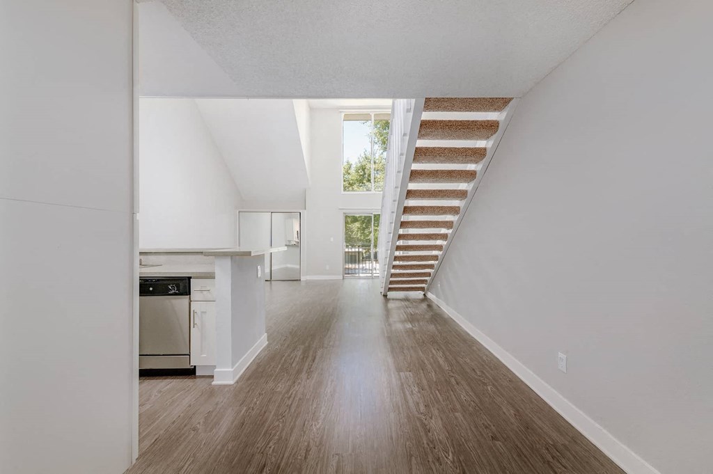 an empty living room with a staircase and a kitchen