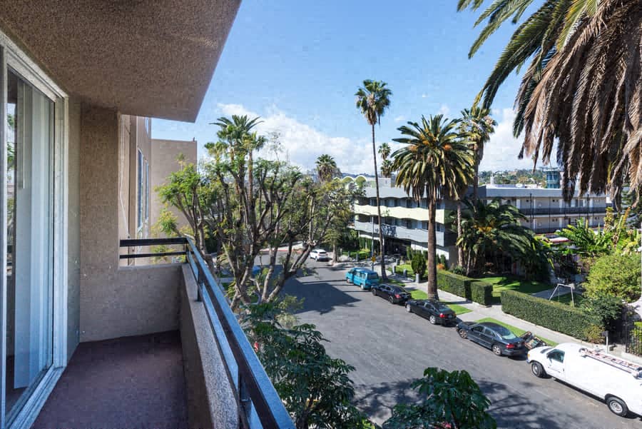 A balcony overlooks a street with cars and palm trees.