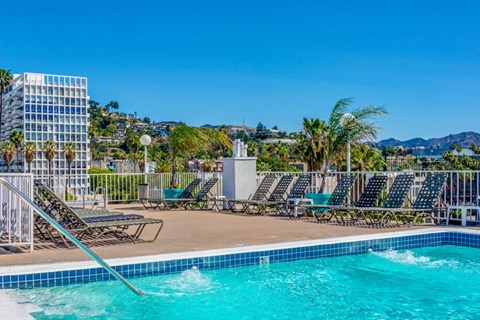 a swimming pool with chaise lounge chairs at a resort with mountains in the background