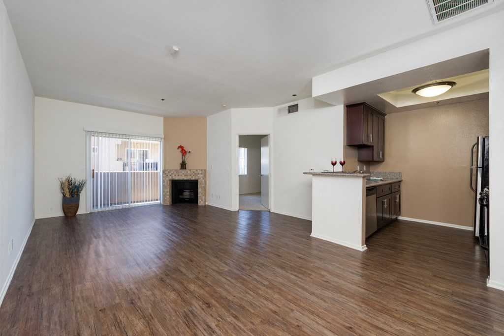 the living room and kitchen of an apartment with wood flooring and a fireplace