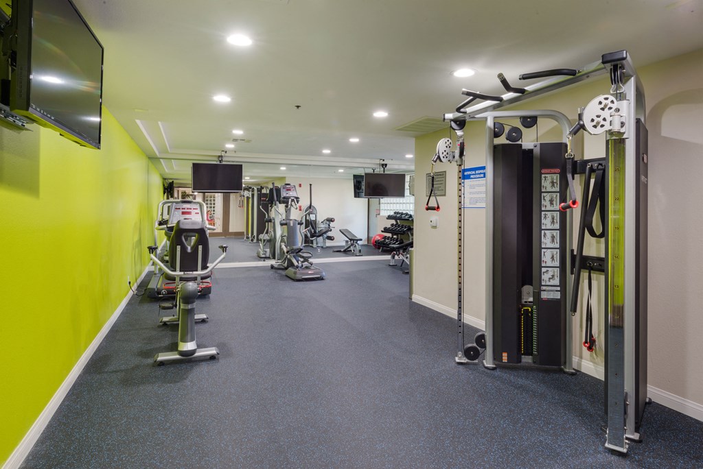 a gym with weights and cardio equipment in a building with yellow walls