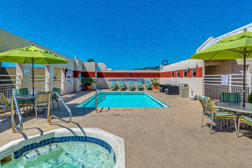 a resort style pool and patio with tables and chairs and umbrellas