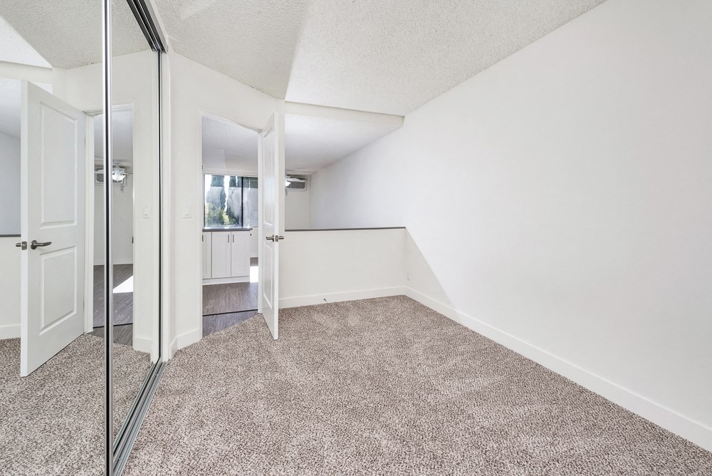 an empty room with white walls and carpet and a mirrored closet