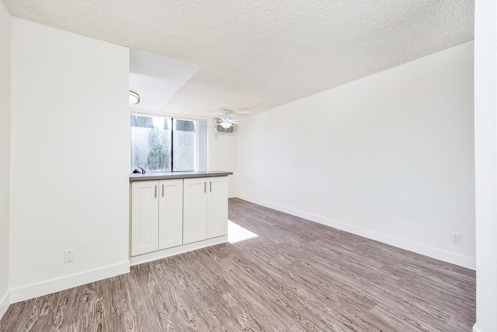 an empty living room and kitchen with white walls and wood flooring