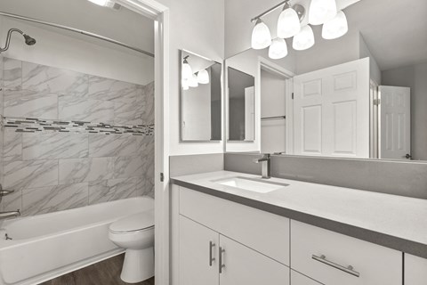 A white bathroom with a marble tile wall and a white tub and toilet.