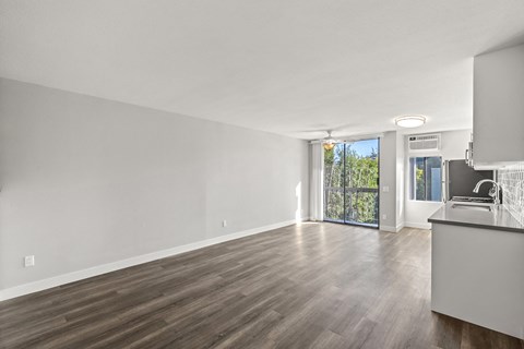 A spacious room with wooden flooring and a kitchen area with white appliances.