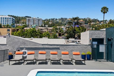 a rooftop pool and lounge chairs on a roof with a city in the background
