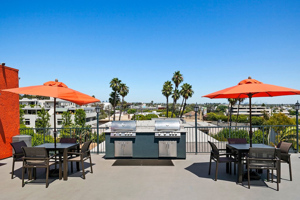 a patio with a barbecue grill and tables with umbrellas